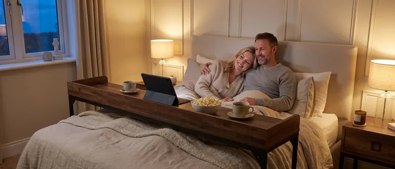 Stel kijkt samen naar een laptop op de DreamDesk tijdens een rustige avond in bed, met popcorn en vier voeten op het dekbed.