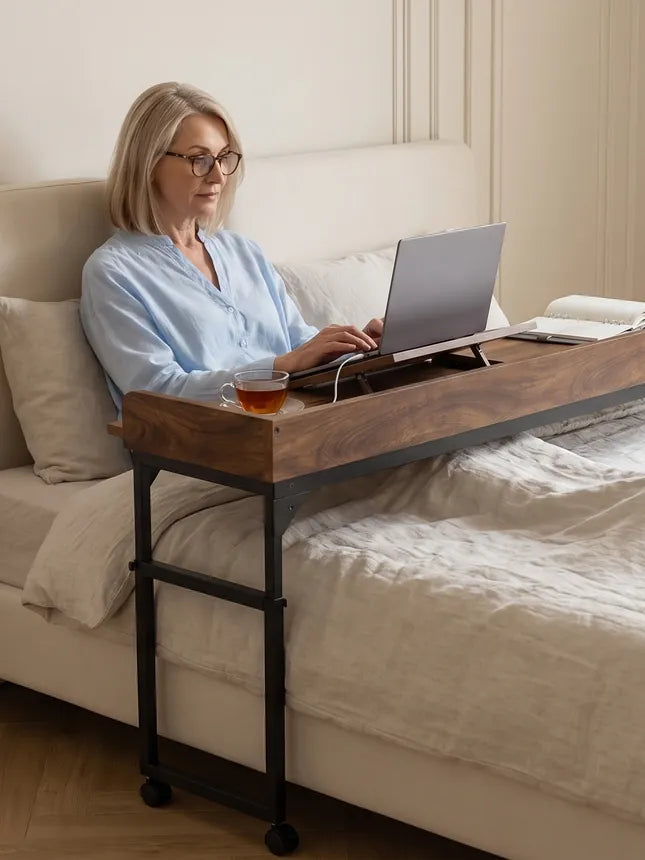 Vrouw zit op bed en gebruikt een laptop op de DreamDesk, met haar benen en sokken op het dekbed.